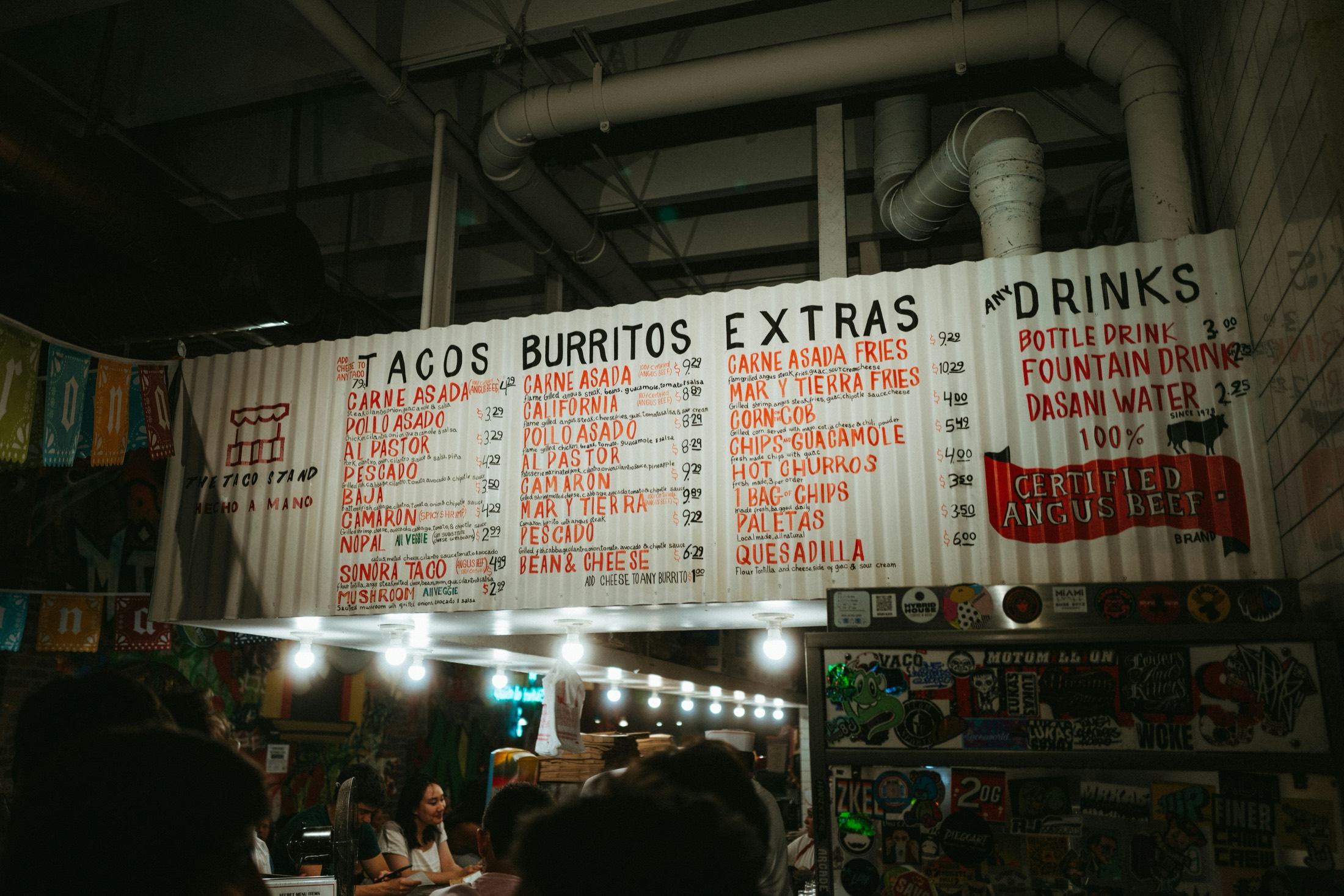 A hand-painted taco stand menu board listing tacos, burritos, and extras