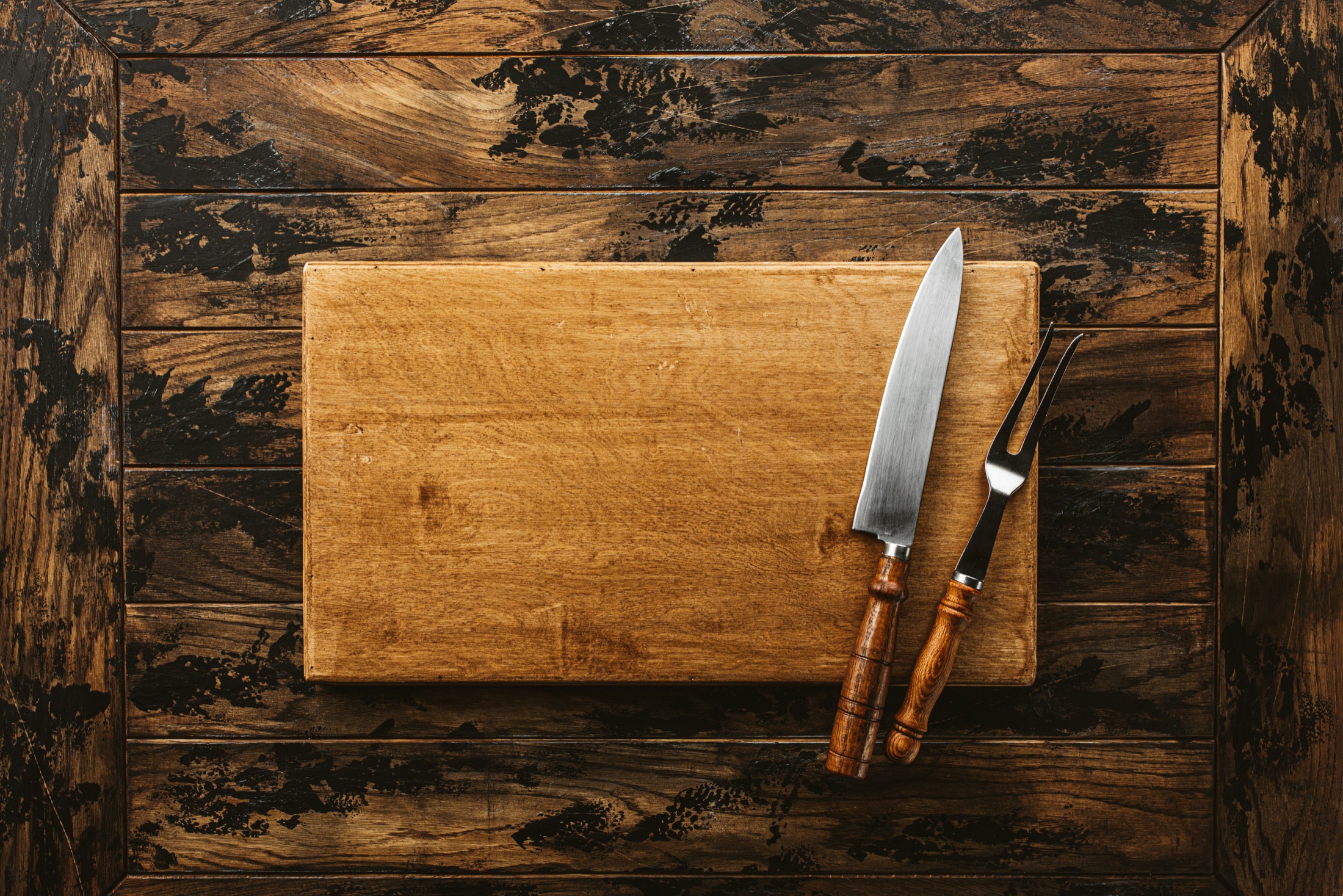 A carving knife and fork resting on a wooden board at a steakhouse